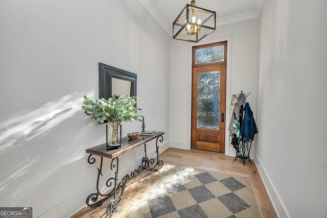 foyer with baseboards, light wood-style floors, a chandelier, and crown molding