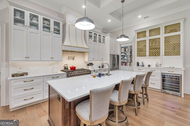 kitchen featuring beverage cooler, premium range hood, light wood-style flooring, a sink, and appliances with stainless steel finishes