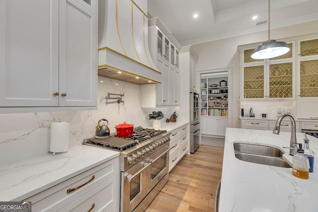 kitchen with custom exhaust hood, a sink, stainless steel appliances, white cabinetry, and light wood-type flooring