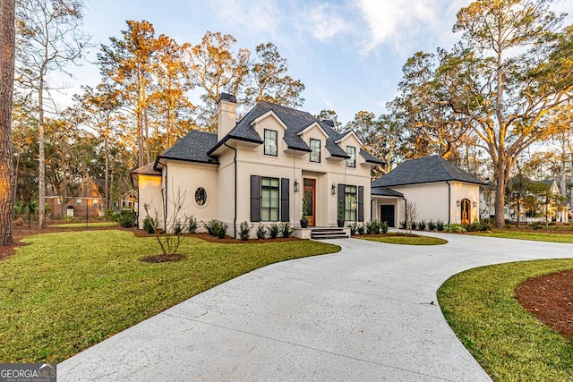 view of front of home featuring a front yard, curved driveway, a chimney, and stucco siding