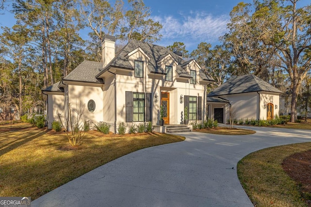 view of front facade with stucco siding, a front lawn, curved driveway, a shingled roof, and a chimney