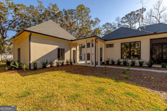 rear view of house featuring stucco siding, a lawn, a patio area, and a shingled roof