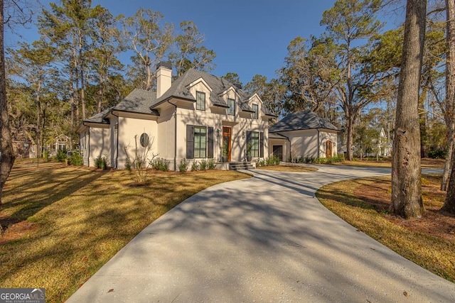 view of front facade featuring stucco siding, a front yard, curved driveway, and a chimney