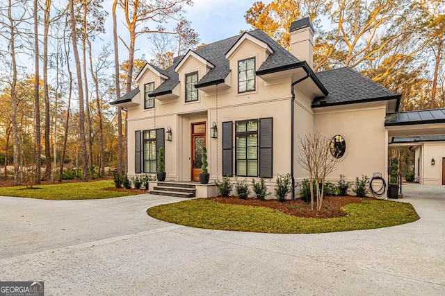 view of front of house featuring stucco siding, a chimney, driveway, and a shingled roof