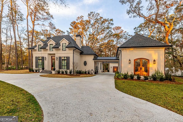 view of front of home featuring a chimney, stucco siding, a front lawn, curved driveway, and french doors