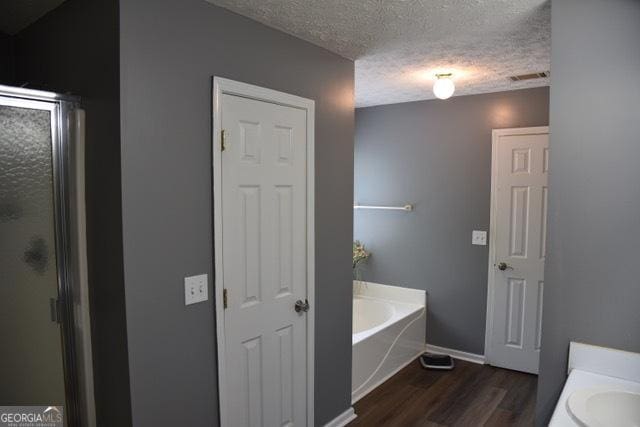 332 Black Willow Ct, Locust Grove, GA 30248 - full bathroom featuring a textured ceiling, wood finished floors, a garden tub, a stall shower, and baseboards