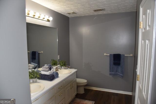 332 Black Willow Ct, Locust Grove, GA 30248 - bathroom with a textured ceiling, double vanity, toilet, wood finished floors, and baseboards