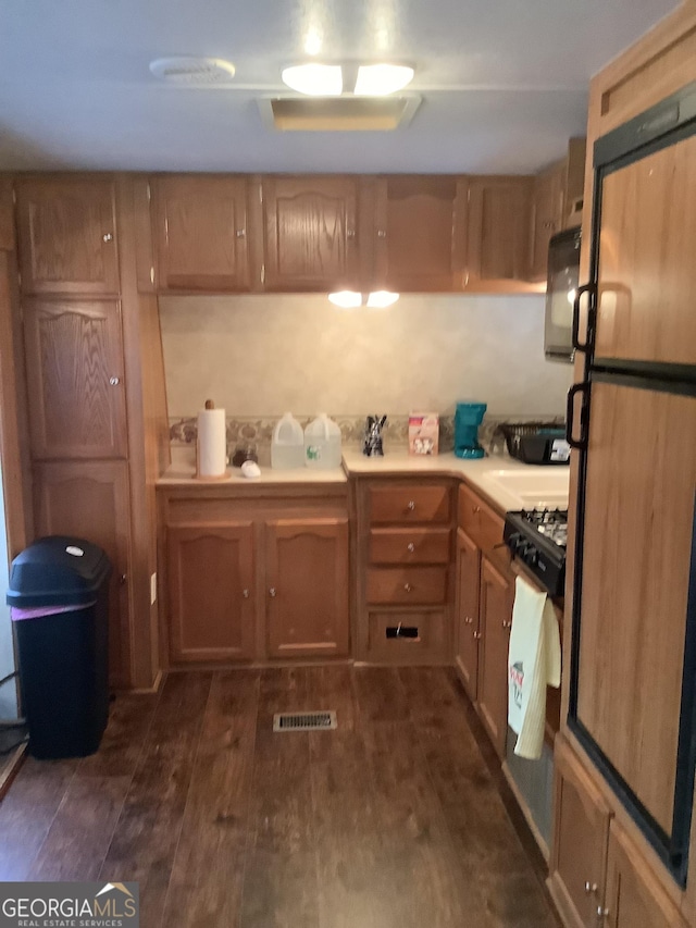 kitchen with brown cabinetry, visible vents, freestanding refrigerator, dark wood-type flooring, and light countertops