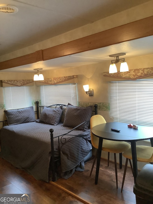 bedroom with beam ceiling, visible vents, and wood finished floors