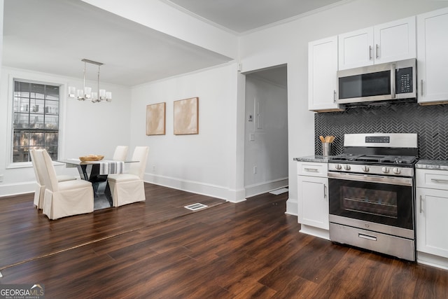 kitchen with tasteful backsplash, ornamental molding, appliances with stainless steel finishes, dark wood-style floors, and a notable chandelier