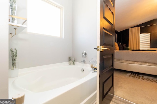 bathroom featuring a bath, ensuite bathroom, and vaulted ceiling