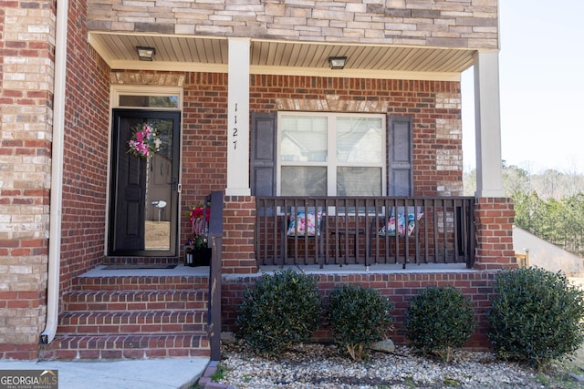 view of exterior entry with brick siding and a porch