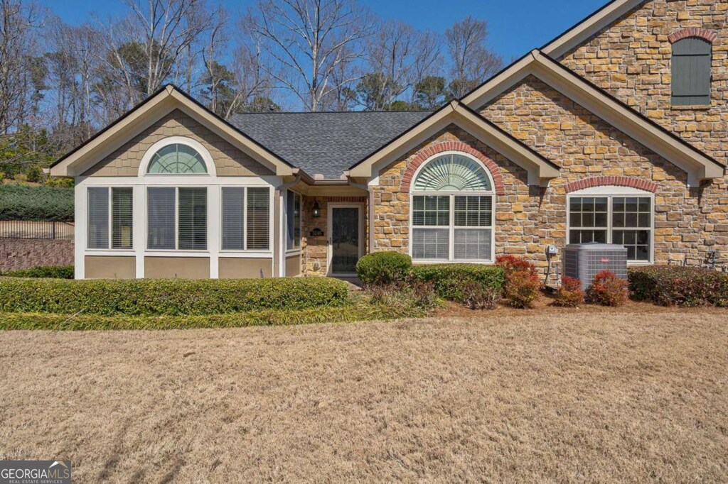 ranch-style house with central air condition unit, stone siding, and a shingled roof