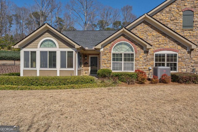 ranch-style house with central air condition unit, stone siding, and a shingled roof
