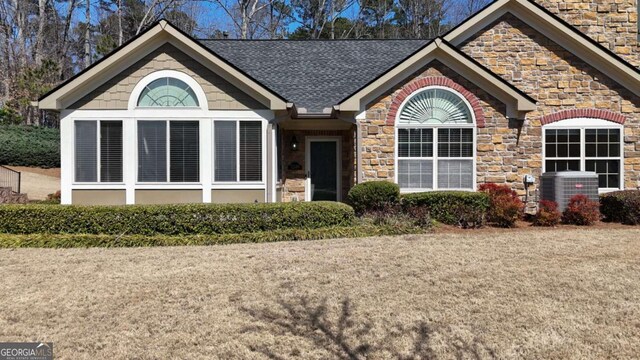 single story home with stone siding, central AC unit, and a shingled roof