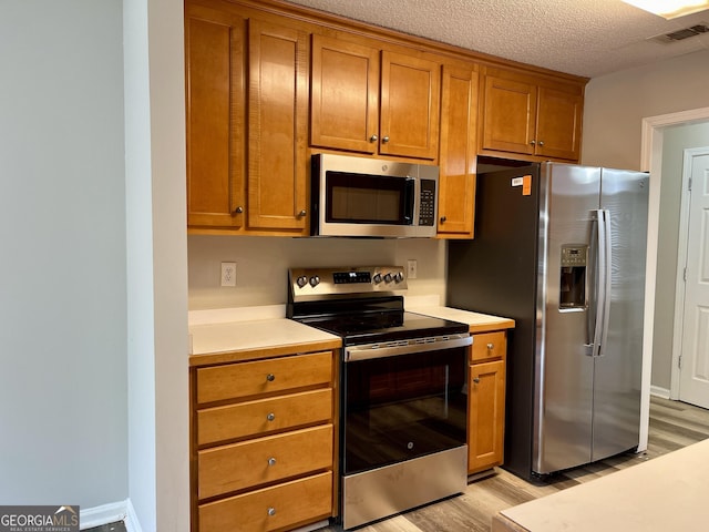 75 Heatherstone Way, Covington, GA 30016 - kitchen featuring appliances with stainless steel finishes, light wood-type flooring, brown cabinetry, light countertops, and a textured ceiling