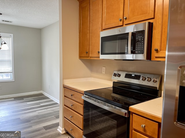 75 Heatherstone Way, Covington, GA 30016 - kitchen with appliances with stainless steel finishes, light wood-type flooring, light countertops, brown cabinetry, and a textured ceiling