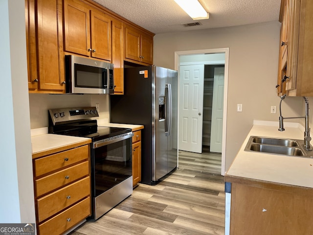 75 Heatherstone Way, Covington, GA 30016 - kitchen featuring stainless steel appliances, light wood-type flooring, brown cabinetry, a textured ceiling, and light countertops