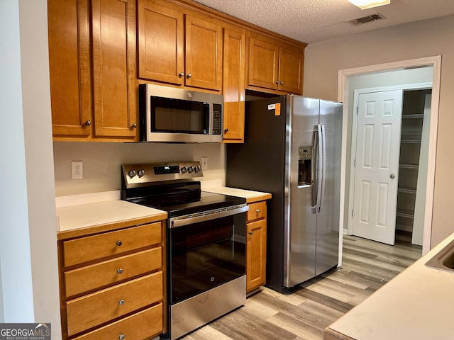 75 Heatherstone Way, Covington, GA 30016 - kitchen featuring appliances with stainless steel finishes, light wood-style floors, brown cabinetry, and light countertops
