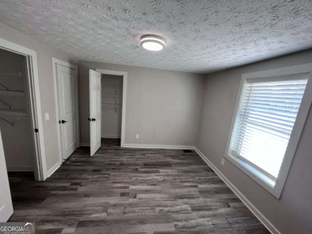 unfurnished bedroom with a textured ceiling, baseboards, and wood finished floors