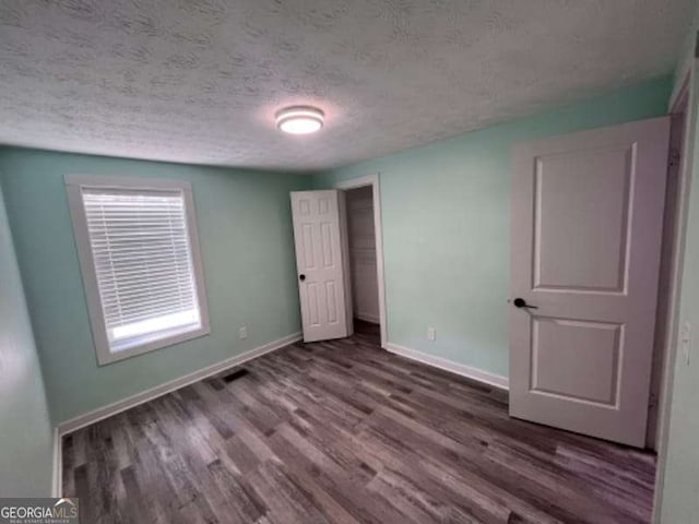 unfurnished bedroom with a closet, baseboards, a textured ceiling, and wood finished floors