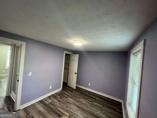 unfurnished bedroom with baseboards, a textured ceiling, and dark wood finished floors