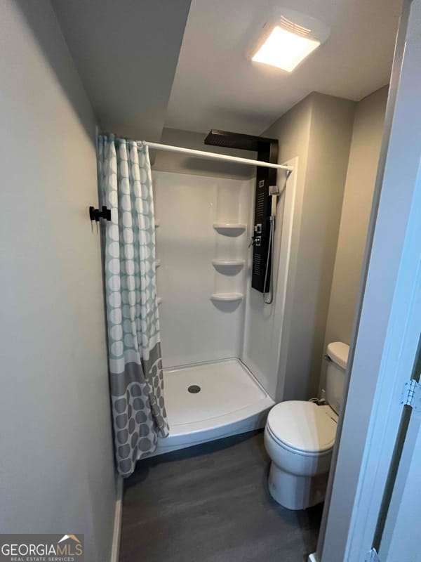 full bathroom featuring a shower stall, toilet, and wood finished floors