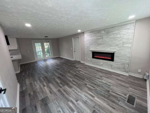 unfurnished living room with visible vents, baseboards, a stone fireplace, wood finished floors, and a textured ceiling