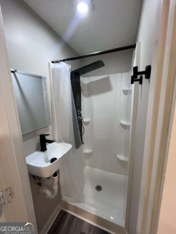 bathroom with a sink, wood finished floors, and a stall shower