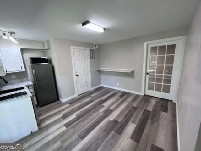 kitchen featuring a sink, stainless steel microwave, wood finished floors, freestanding refrigerator, and white cabinets