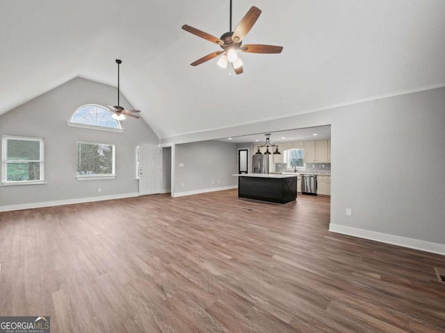 unfurnished living room featuring ceiling fan with notable chandelier, high vaulted ceiling, baseboards, and wood finished floors