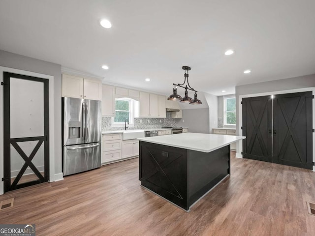 kitchen with a sink, decorative backsplash, light countertops, light wood-style floors, and appliances with stainless steel finishes