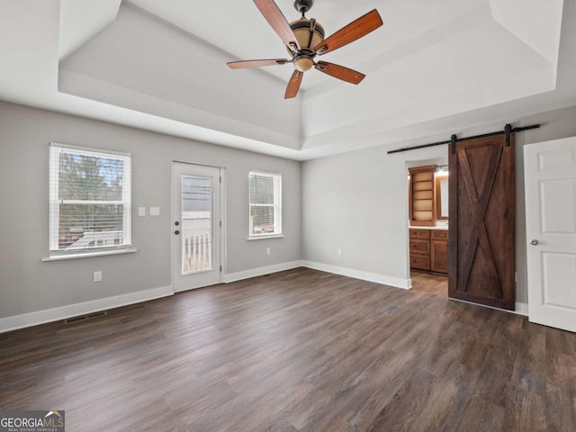 unfurnished living room featuring visible vents, a tray ceiling, a barn door, ceiling fan, and dark wood-style flooring