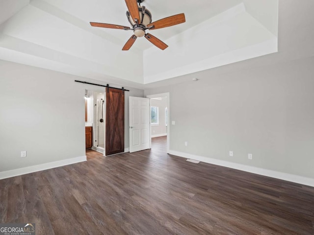 unfurnished room featuring ceiling fan, baseboards, a barn door, a tray ceiling, and dark wood-style flooring