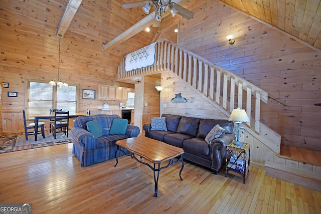 living room with beamed ceiling, ceiling fan with notable chandelier, light wood-style floors, wood walls, and wooden ceiling