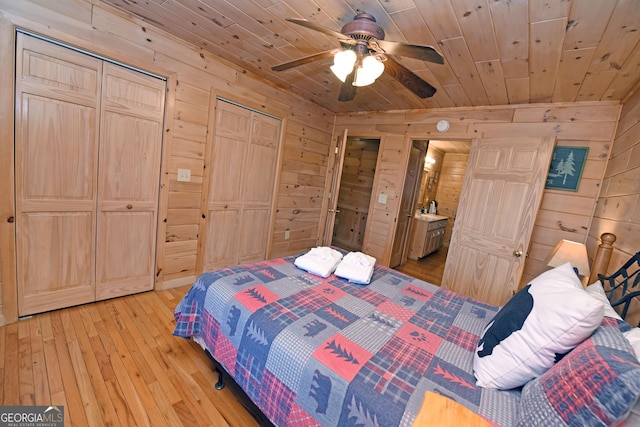 bedroom with two closets, wooden walls, light wood finished floors, wood ceiling, and ceiling fan