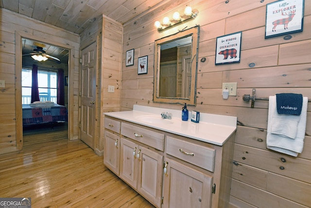 ensuite bathroom with wood walls, wood ceiling, vanity, a ceiling fan, and wood-type flooring