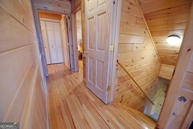 hall featuring light wood finished floors, wood walls, and wood ceiling