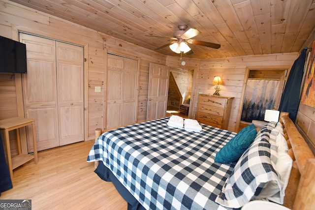 bedroom featuring ceiling fan, multiple closets, wood walls, wooden ceiling, and light wood-type flooring