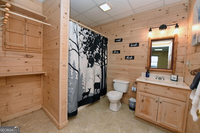 bathroom with vanity, wooden walls, a shower with curtain, a drop ceiling, and toilet