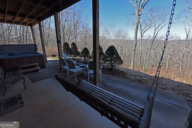 view of patio with a forest view and a hot tub