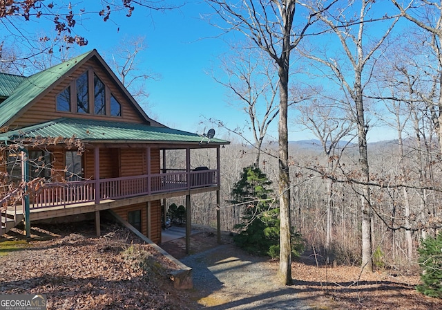 exterior space featuring log veneer siding, metal roof, a wooden deck, and driveway