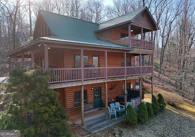 back of house featuring log veneer siding, metal roof, and covered porch