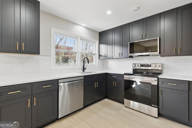 kitchen with a sink, stainless steel appliances, light wood-style floors, light countertops, and decorative backsplash