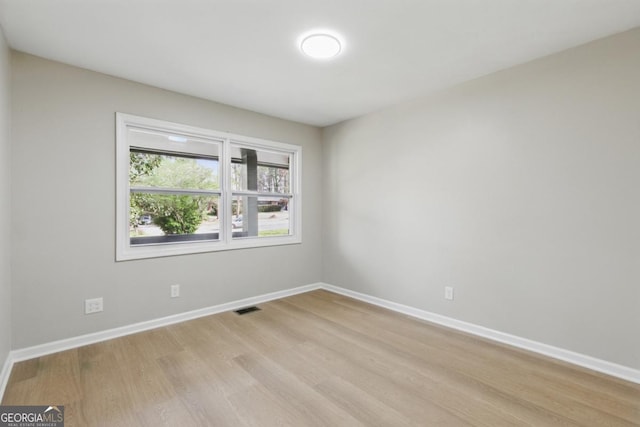 spare room featuring light wood-type flooring, visible vents, and baseboards