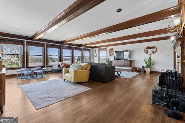 living area featuring visible vents, beam ceiling, a healthy amount of sunlight, and wood finished floors