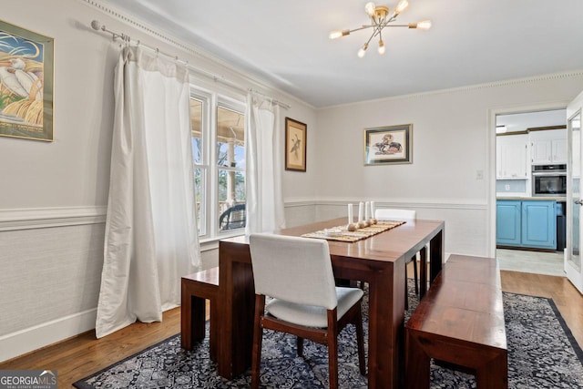 dining area featuring a chandelier, a wainscoted wall, crown molding, and light wood-style floors