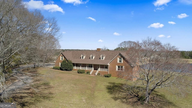 view of front of house with brick siding, covered porch, a chimney, and a front lawn