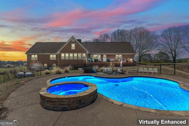 pool at dusk featuring a patio area, a pool with connected hot tub, and fence