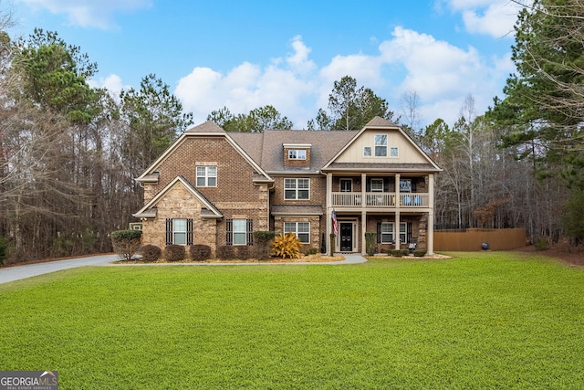 view of front of house featuring a front lawn, a balcony, brick siding, and roof with shingles